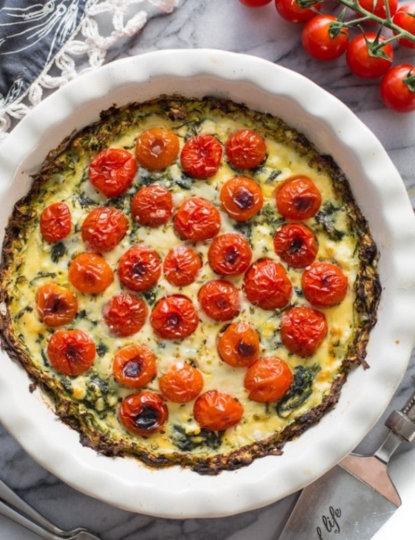 Zucchini Crust Tomato Spinach Feta Quiche in a pie plate on a marble counter top