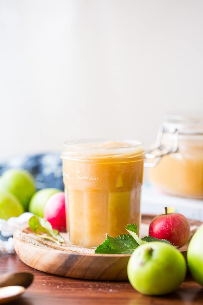 Instant Pot applesauce in a jar on a wooden plate surrounded by red and green apples 