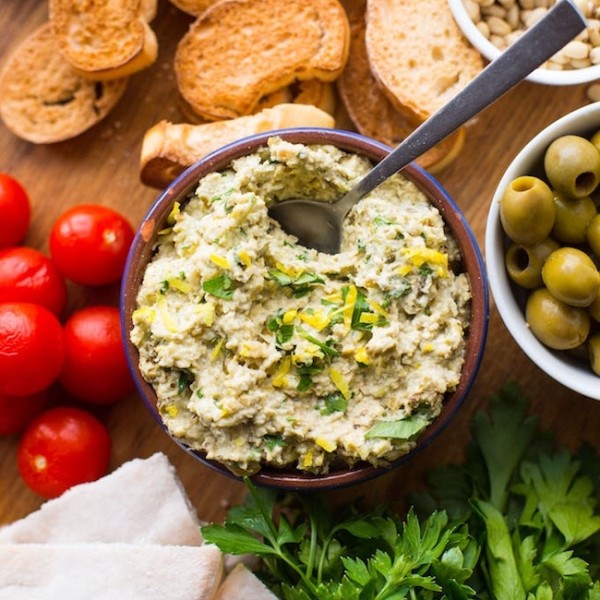 green olive tapenade on a serving board surrounded by veggies, crostini and pita