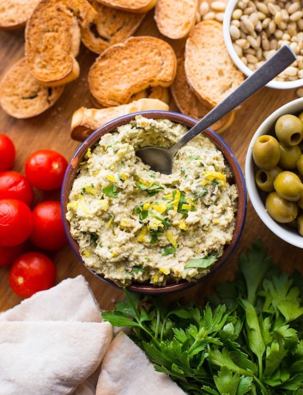 green olive tapenade on a serving board surrounded by veggies, crostini and pita