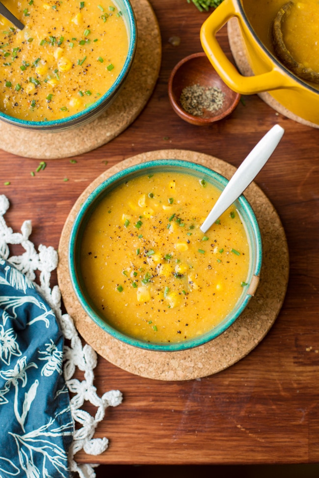 vegan corn chowder in a green bowl topped with fresh chopped chives