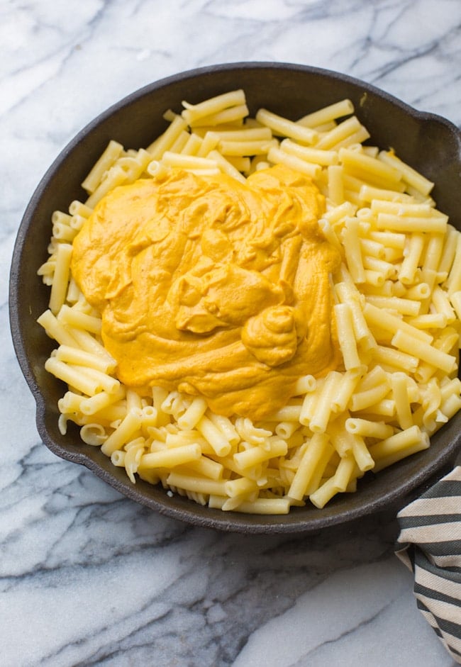 pumpkin mac and cheese sauce poured over cooked macaroni in a cast iron skillet