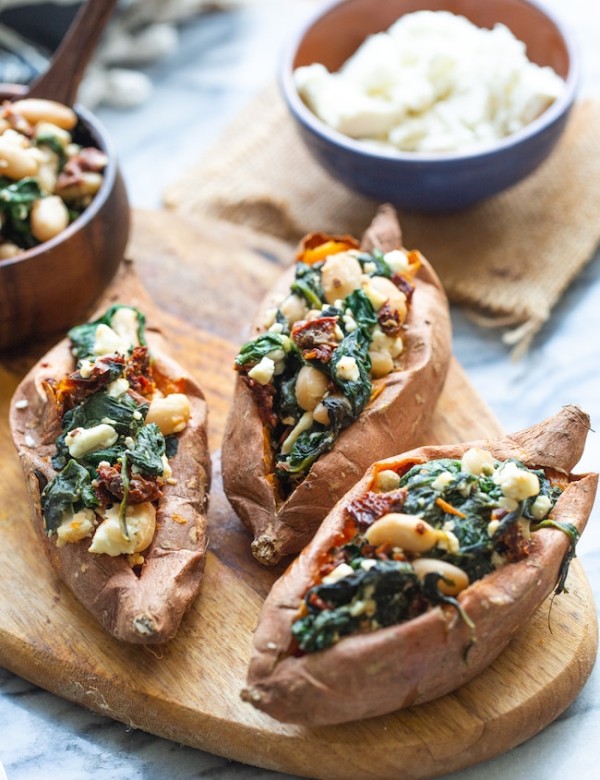 Spinach and Feta Stuffed Sweet Potatoes on a wooden cutting board with feta