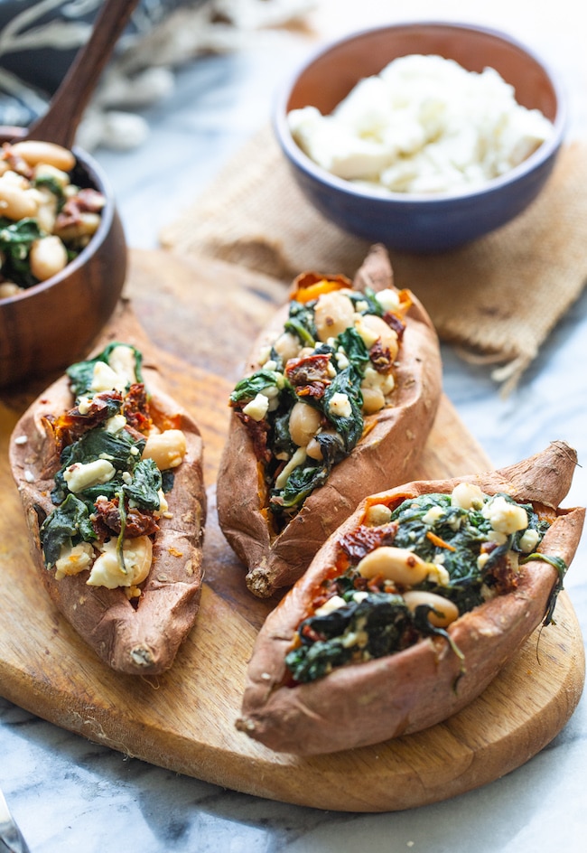 Spinach and Feta Stuffed Sweet Potatoes on a wooden cutting board with feta