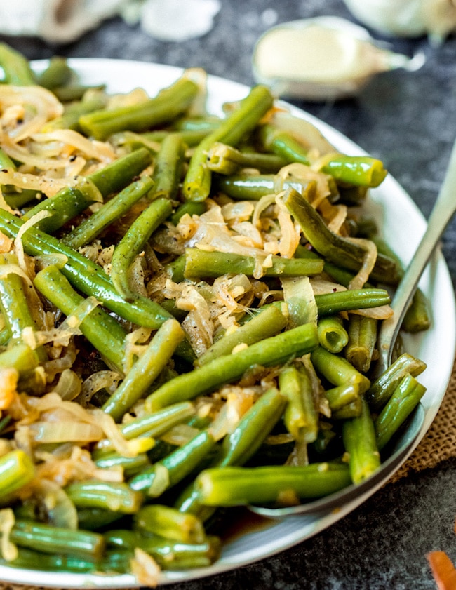 stir fried green beans on a plate with a serving spoon