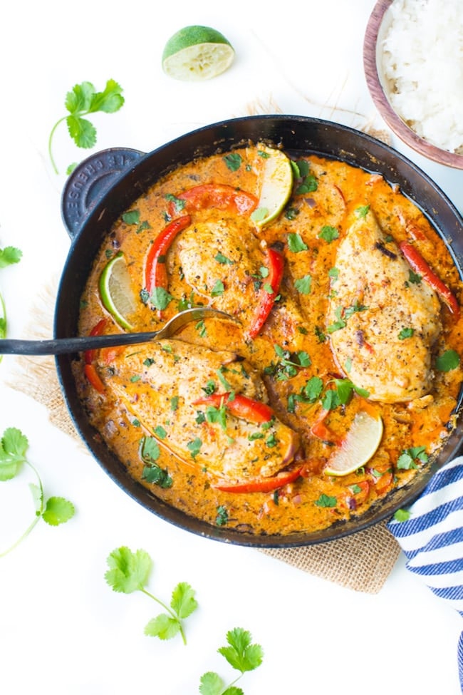 Thai Red Coconut Chicken in a skillet topped with limes and fresh cilantro