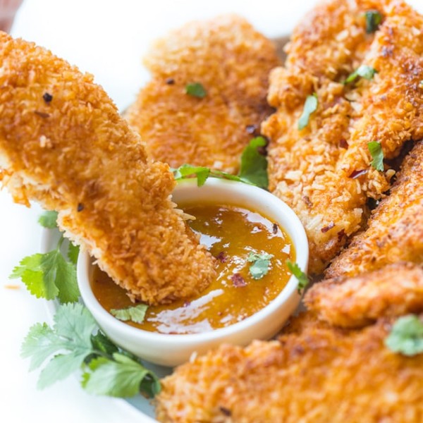 Coconut Crusted Chicken Tenders dipping into a sauce