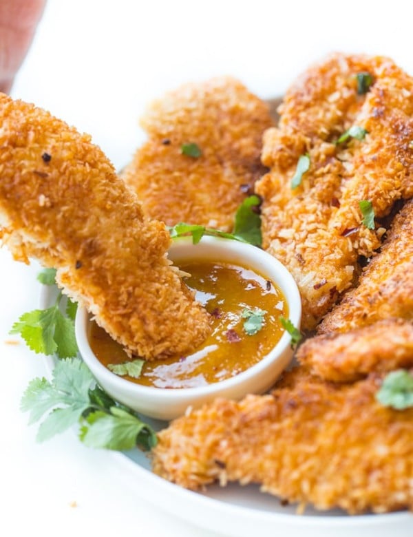 Coconut Crusted Chicken Tenders dipping into a sauce