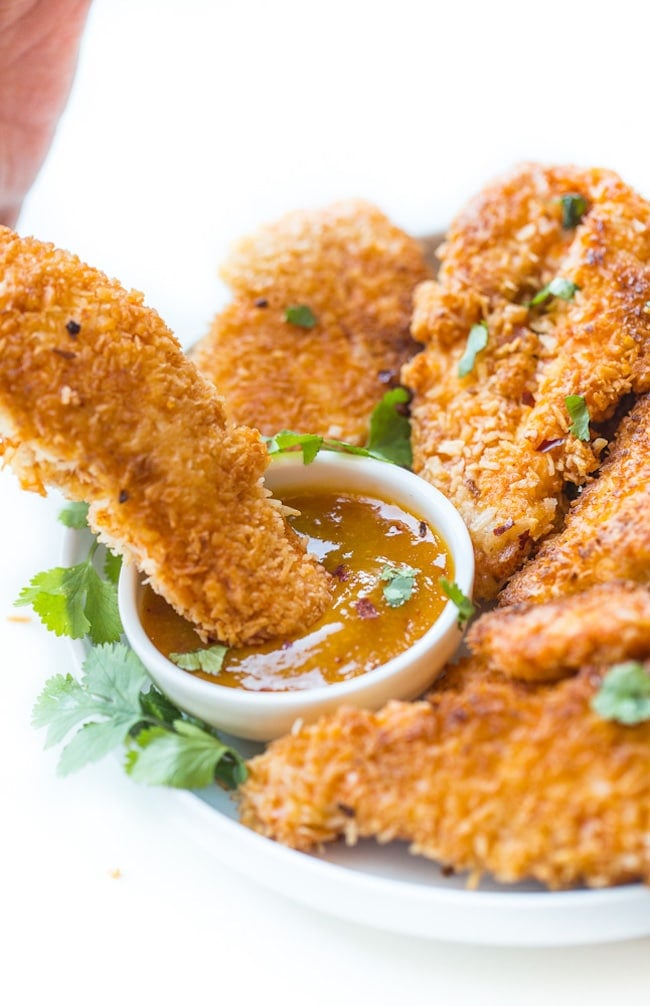 Coconut Crusted Chicken Tenders dipping into a sauce