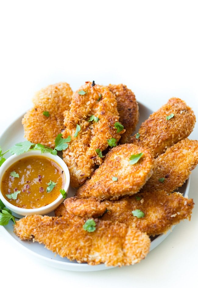 Coconut Crusted Chicken Tenders on a plate with a dipping sauce