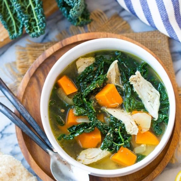 Kale & Sweet Potato Instant Pot Chicken Soup in a bowl on a wooden plate next to kale