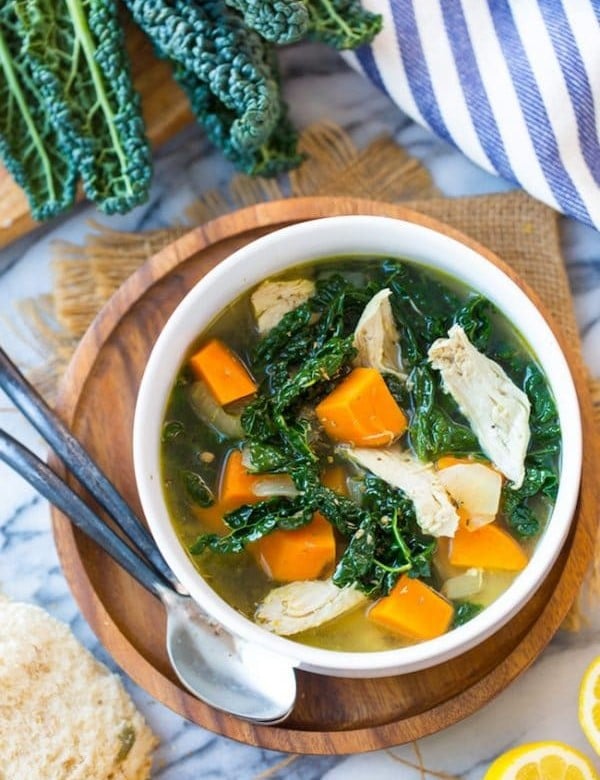 Kale & Sweet Potato Instant Pot Chicken Soup in a bowl on a wooden plate next to kale