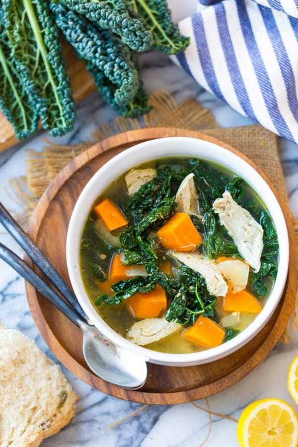 Kale & Sweet Potato Instant Pot Chicken Soup in a bowl on a wooden plate next to kale