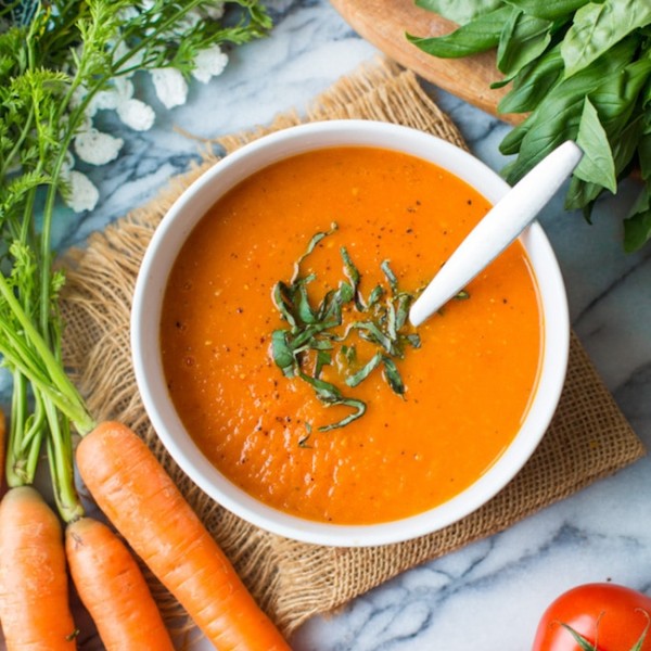 Low FODMAP Carrot Tomato Soup topped with fresh basil and surrounded by produce