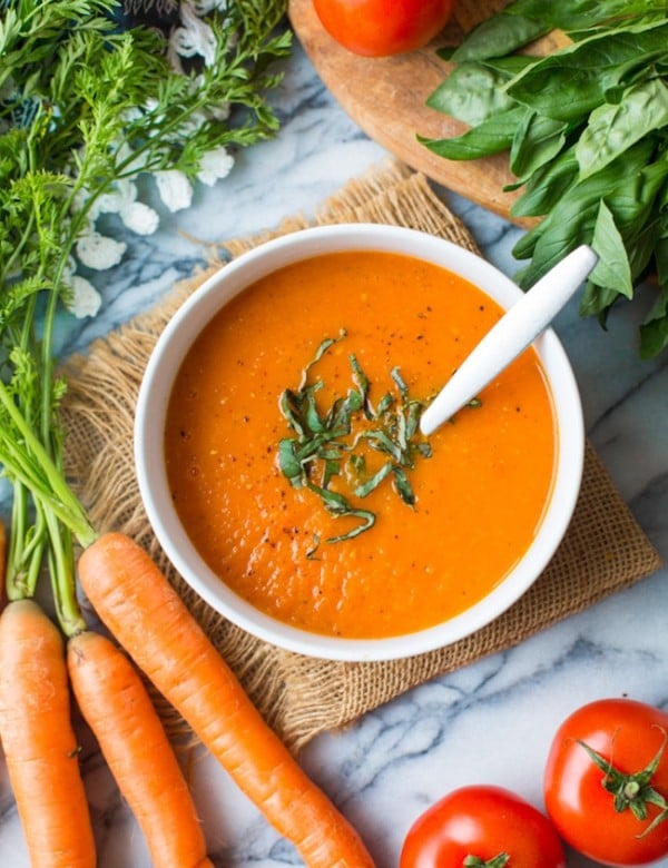 Low FODMAP Carrot Tomato Soup topped with fresh basil and surrounded by produce