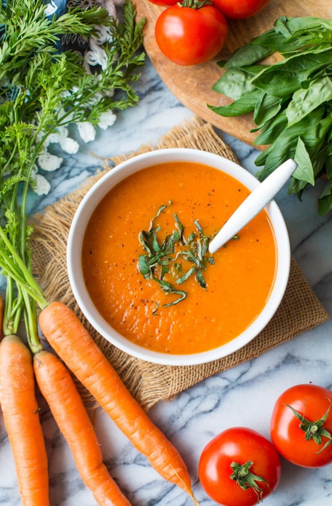 Low FODMAP Carrot Tomato Soup topped with fresh basil and surrounded by produce