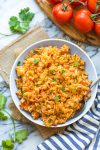 Mexican Rice in a bowl surrounded by tomatoes and cilantro