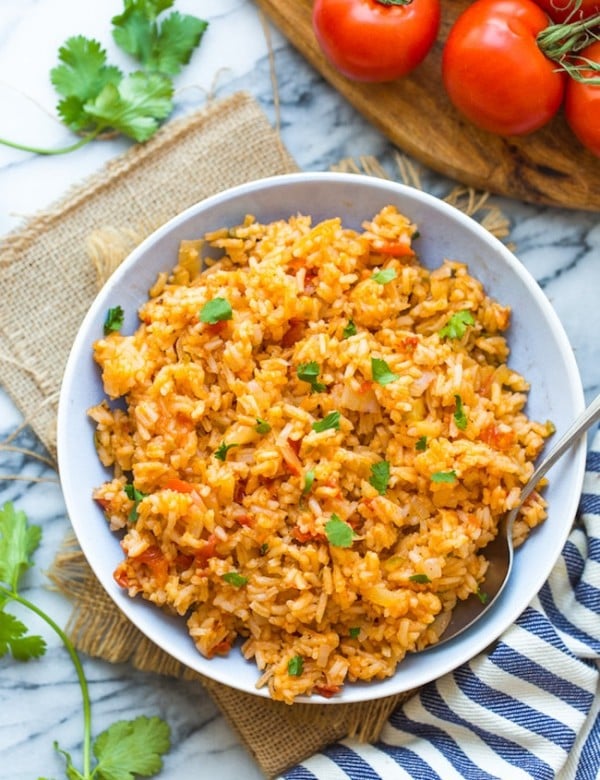 Mexican Rice in a bowl surrounded by tomatoes and cilantro