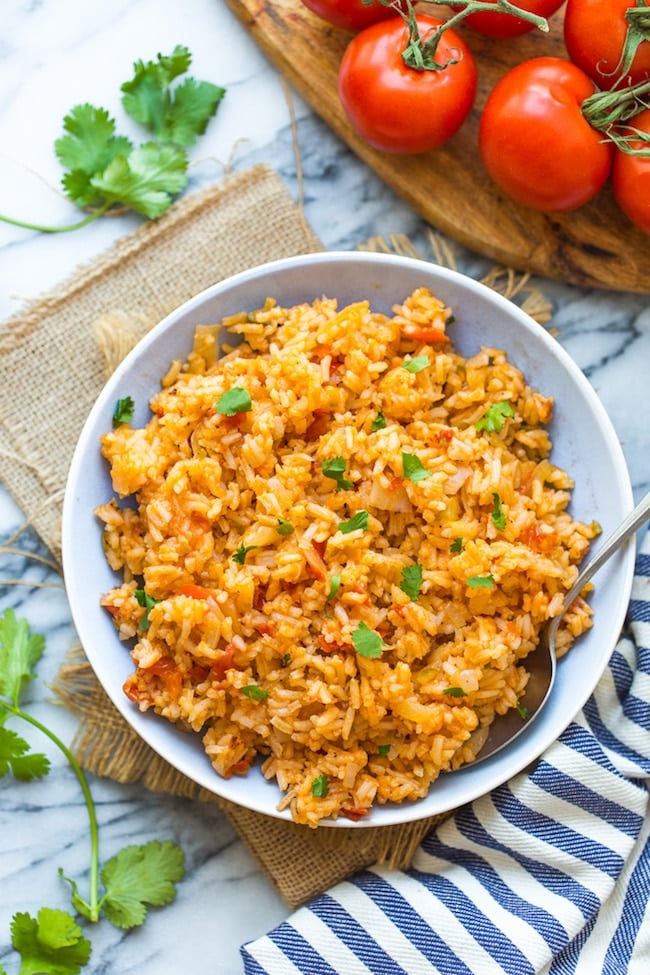 Mexican red Rice in a bowl surrounded by tomatoes and cilantro 