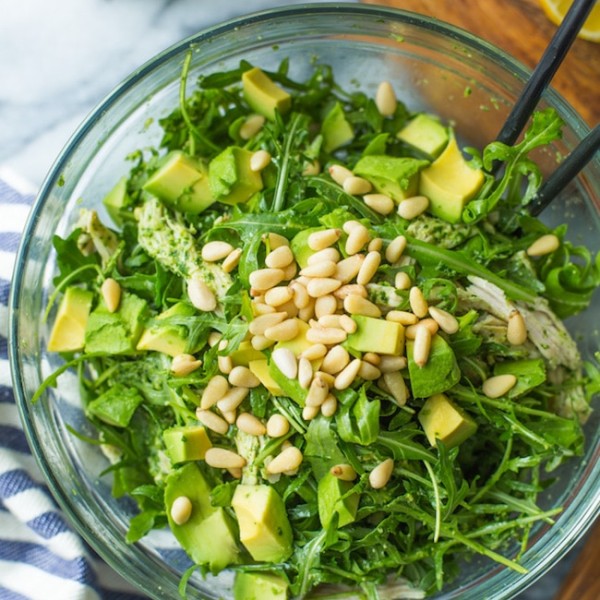 chicken pesto salad in a glass bowl topped with pine nuts