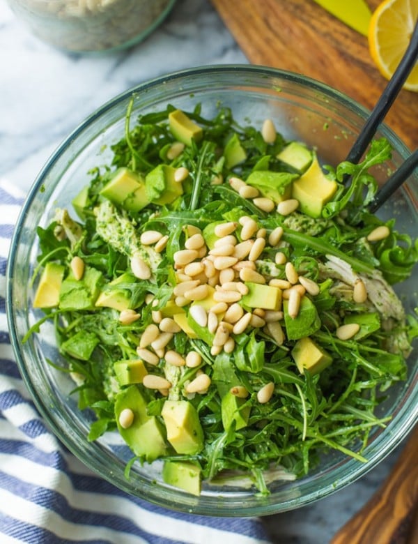 chicken pesto salad in a glass bowl topped with pine nuts