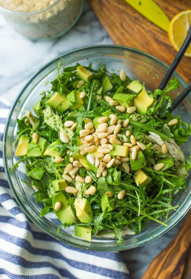 chicken pesto salad in a glass bowl topped with pine nuts