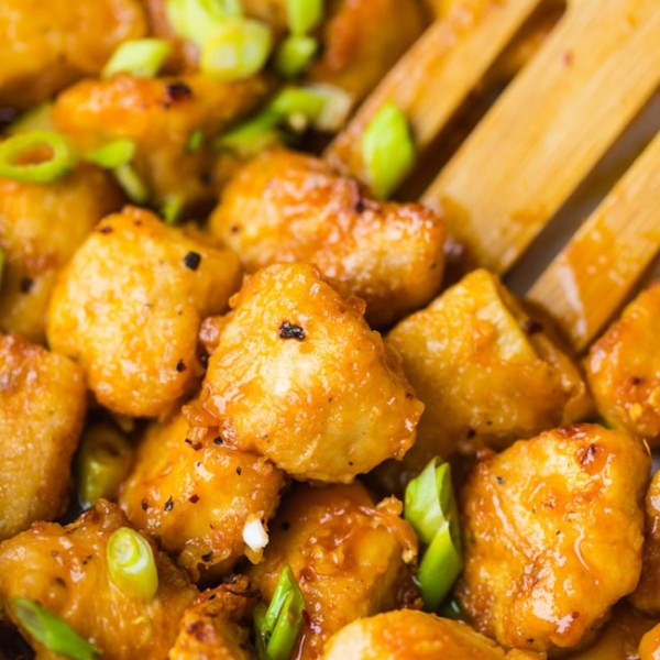 paleo fire cracker chicken topped with chopped spring onions stirred by a wooden spoon