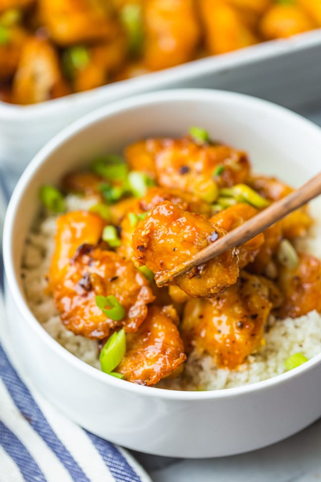 paleo firecracker chicken in a bowl with cauliflower rice - chopsticks holding a piece up