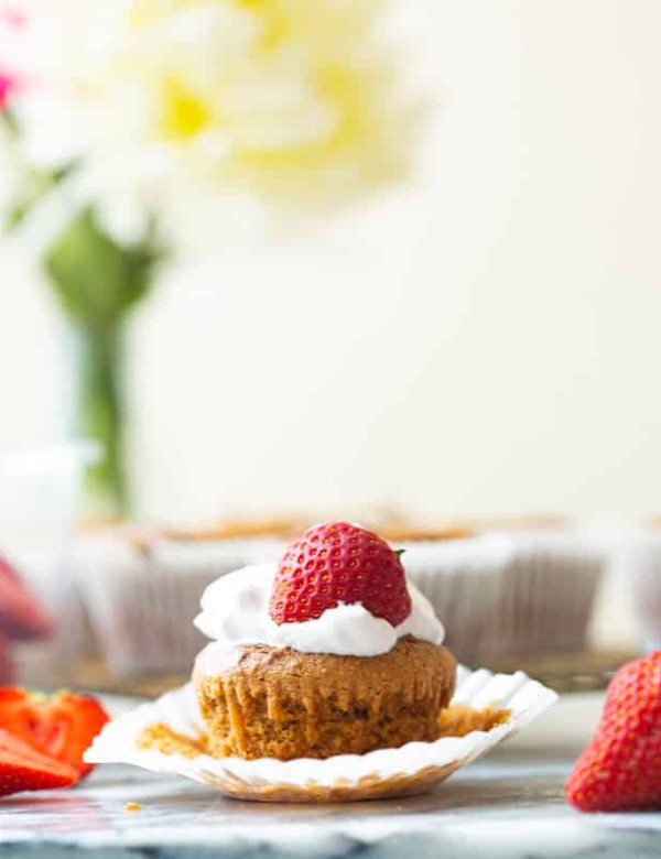 Paleo-Vegan-Cupcakes surrounded by fresh strawberries - one cupcake topped with whipped cream and a strawberry with the paper liner pulled back