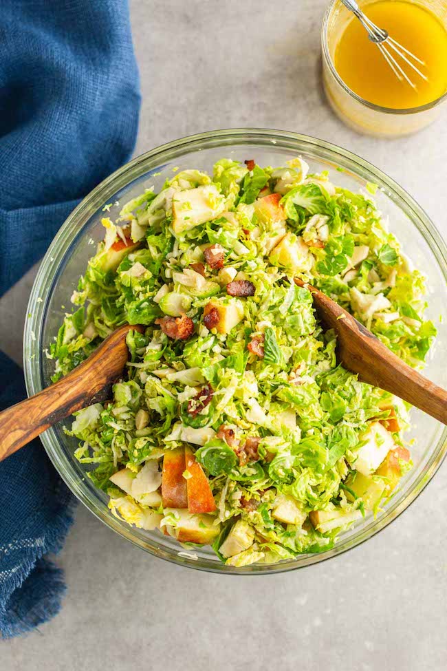 Shaved Brussels Sprouts Salad with Apples & Honey Mustard Vinaigrette in a salad bowl with wooden tongs