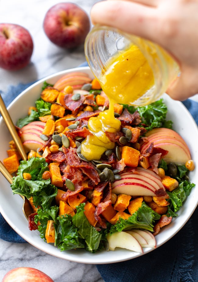 Roasted Sweet Potato & Chickpea Kale Apple Salad with Bacon with the maple mustard vinaigrette pouring over top 
