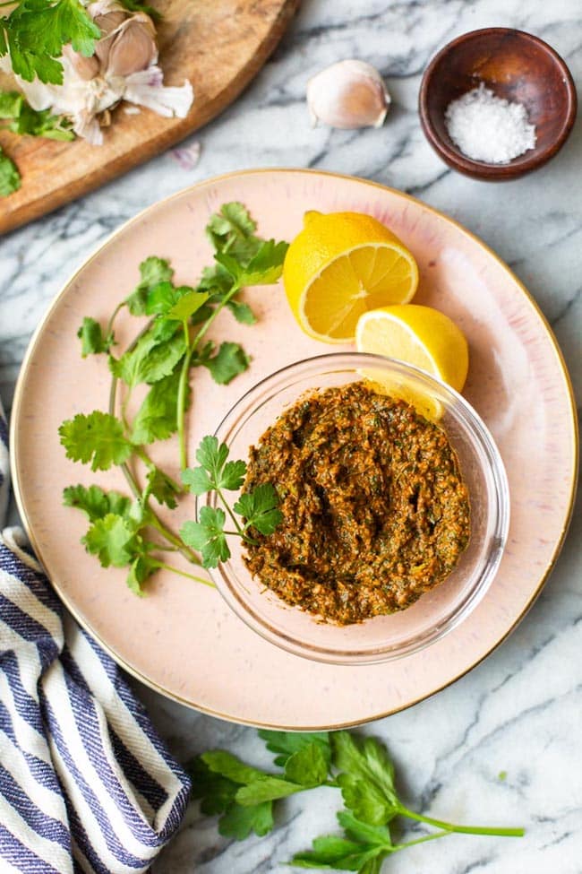Chermoula-Paste on a pink plate surrounded by herbs