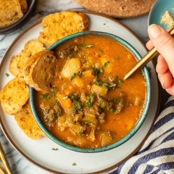 a hand taking a spoonful of Tomato-y & Kale White Bean Soup