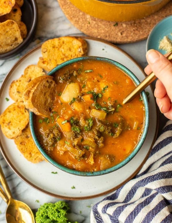 a hand taking a spoonful of Tomato-y & Kale White Bean Soup