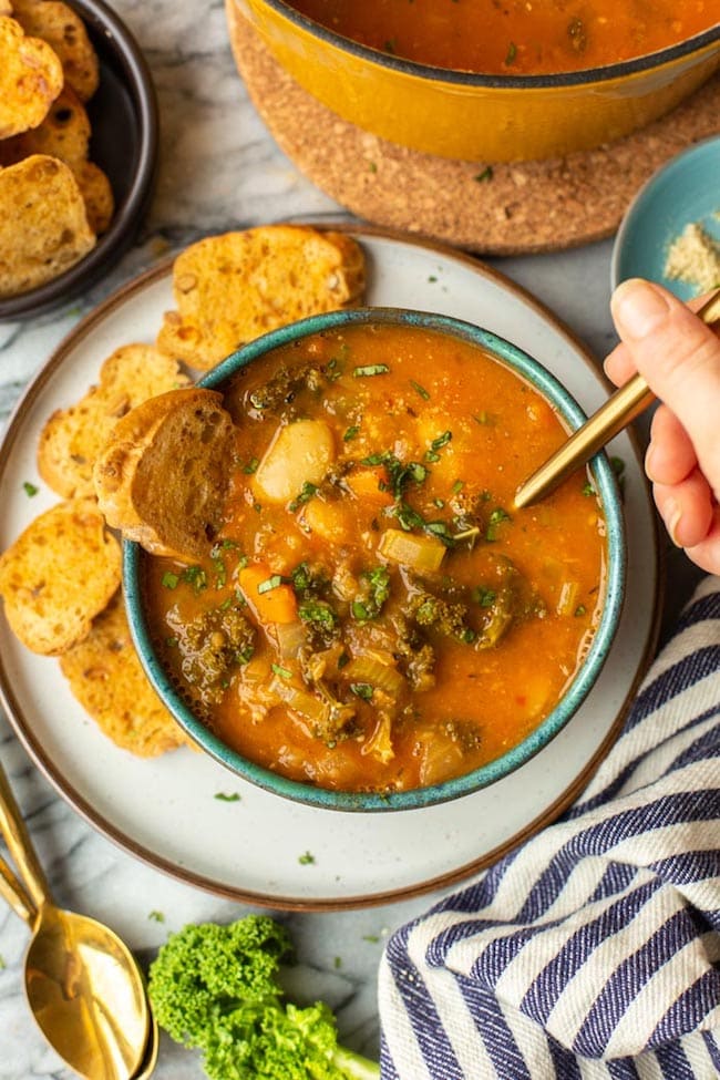 a hand taking a spoonful of Tomato-y & Kale White Bean Soup