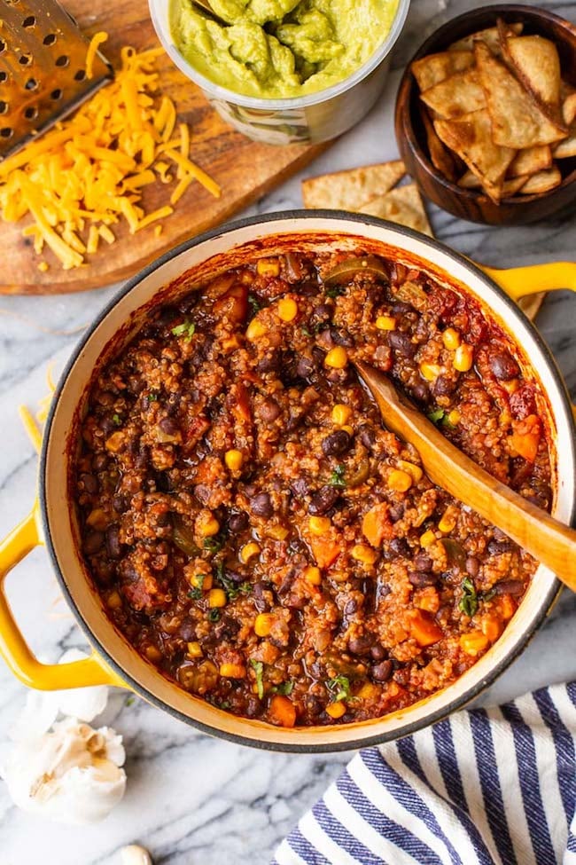 Black Bean Quinoa Veggie Chili in a large yellow cooking pot surrounded by guac and cheese