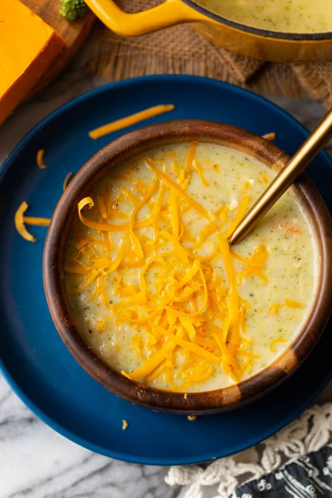 broccoli potato soup in a wood bowl on a blue plate
topped with cheese