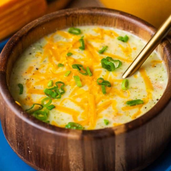 broccoli potato soup in a wood bowl topped with cheese and spring onions