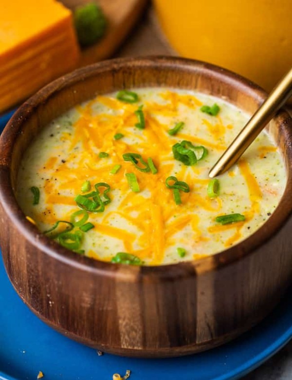 broccoli potato soup in a wood bowl topped with cheese and spring onions