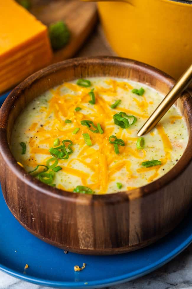 broccoli potato soup in a wood bowl topped with cheese and spring onions