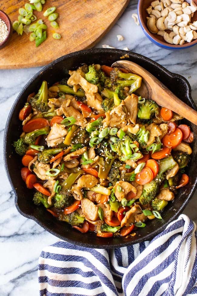 Salteado de Brócoli de pollo Teriyaki en una sartén de hierro fundido con un paño de cocina a rayas azules y blancas