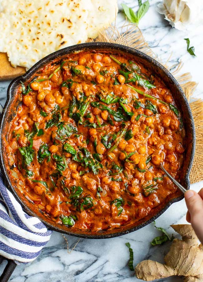 hand scooping Tomato Basil Coconut Chickpea Curry in a cast iron skillet