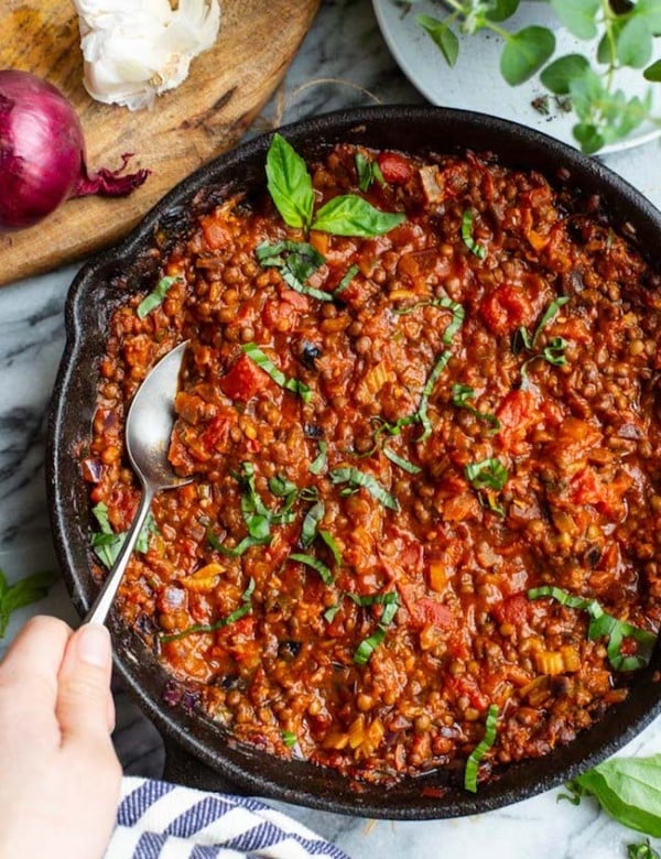 A hand scooping out a spoonful of Vegetarian Lentil Bolognese