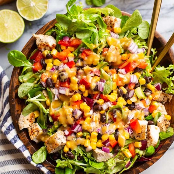 southwest chicken salad with chopped red pepper, red onion, corn, black beans and chicken tossed in a salad bowl and covered with tahini dressing