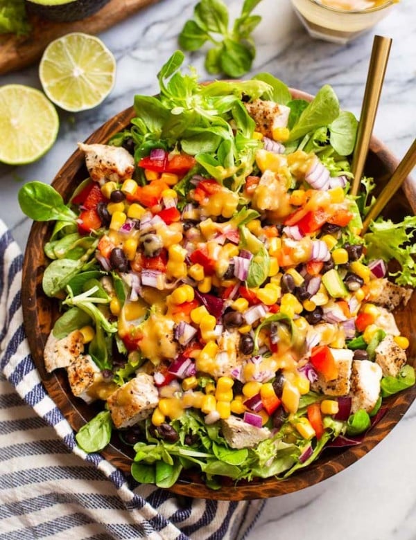 southwest chicken salad with chopped red pepper, red onion, corn, black beans and chicken tossed in a salad bowl and covered with tahini dressing