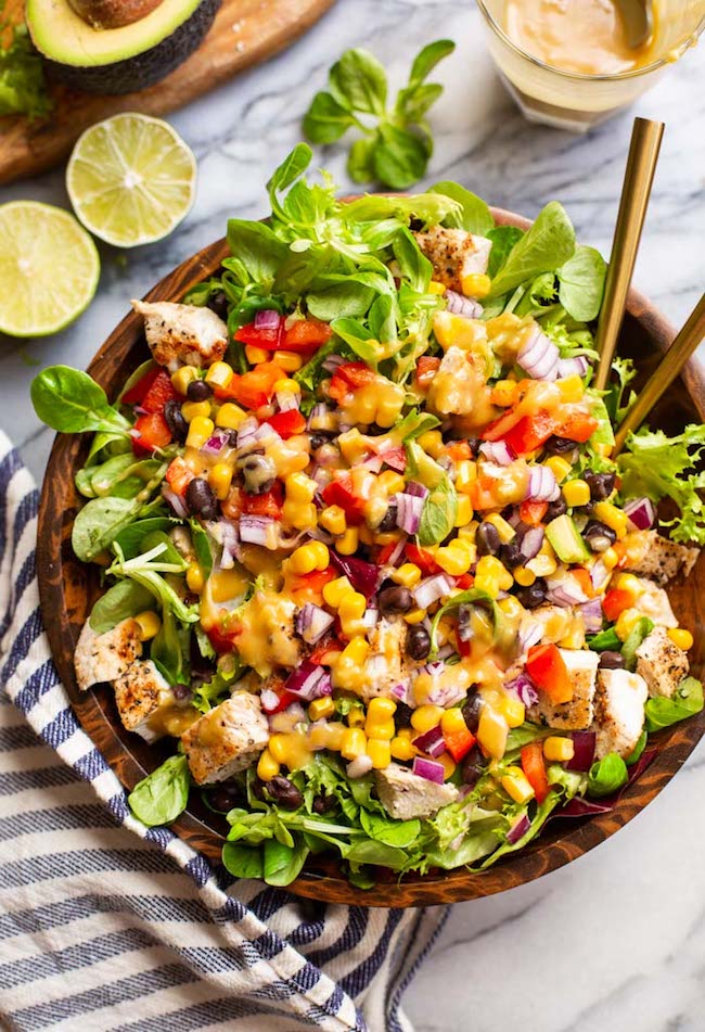 southwest chicken salad with chopped red pepper, red onion, corn, black beans and chicken tossed in a salad bowl and covered with tahini dressing