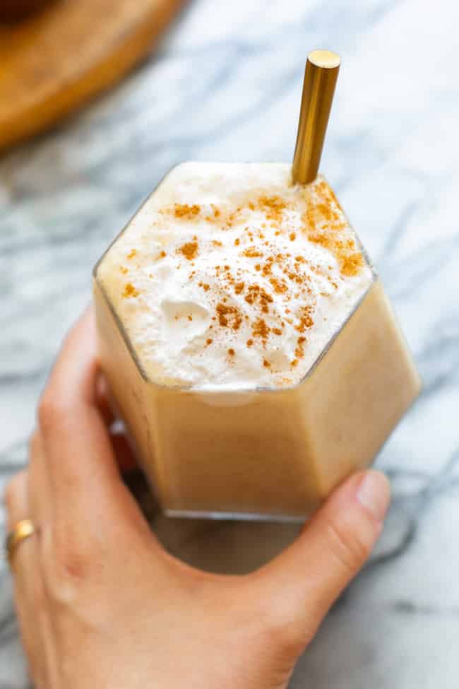 homemade chai frappuccino with a straw topped with vegan whipped cream and a sprinkling of cinnamon