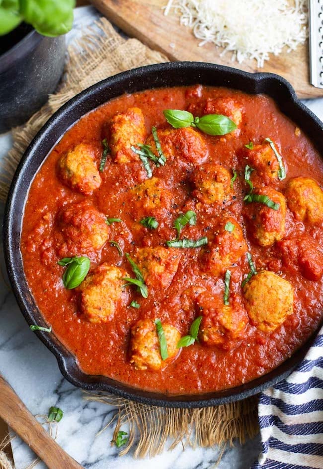 Healthy Chicken Meatballs in a cast iron skillet topped with basil and black pepper
