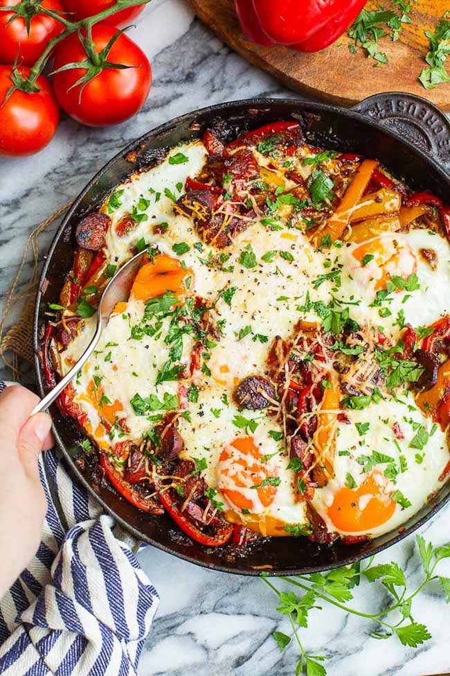 Baked Chorizo & Eggs with Peperonata in a skillet with a hand scooping some up