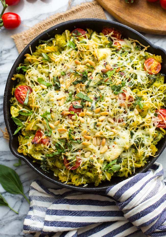 baked vegan pesto pasta in a cast iron skillet topped with sliced basil and pine nuts 